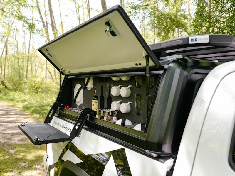 RLD stainless steel truck cap with upgraded kitchen cabinet shown open with fold down table and dishware embedded in foam storage insert