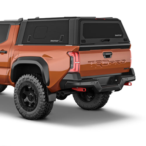 Rear three-quarter view of an orange Toyota Tacoma pickup truck with a black Smart Cap canopy cover on the bed, black rear bumper and diffuser, and black off-road tires on a white studio background.