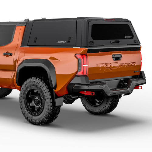 Rear three-quarter view of an orange Toyota Tacoma pickup truck with a black Smart Cap canopy cover on the bed, black rear bumper and diffuser, and black off-road tires on a white studio background.