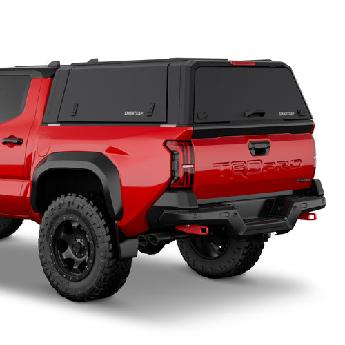 Rear three-quarter view of a red Toyota Tacoma pickup truck with a black Smart Cap canopy cover on the bed, black rear bumper and diffuser, and black off-road tires on a white studio background.