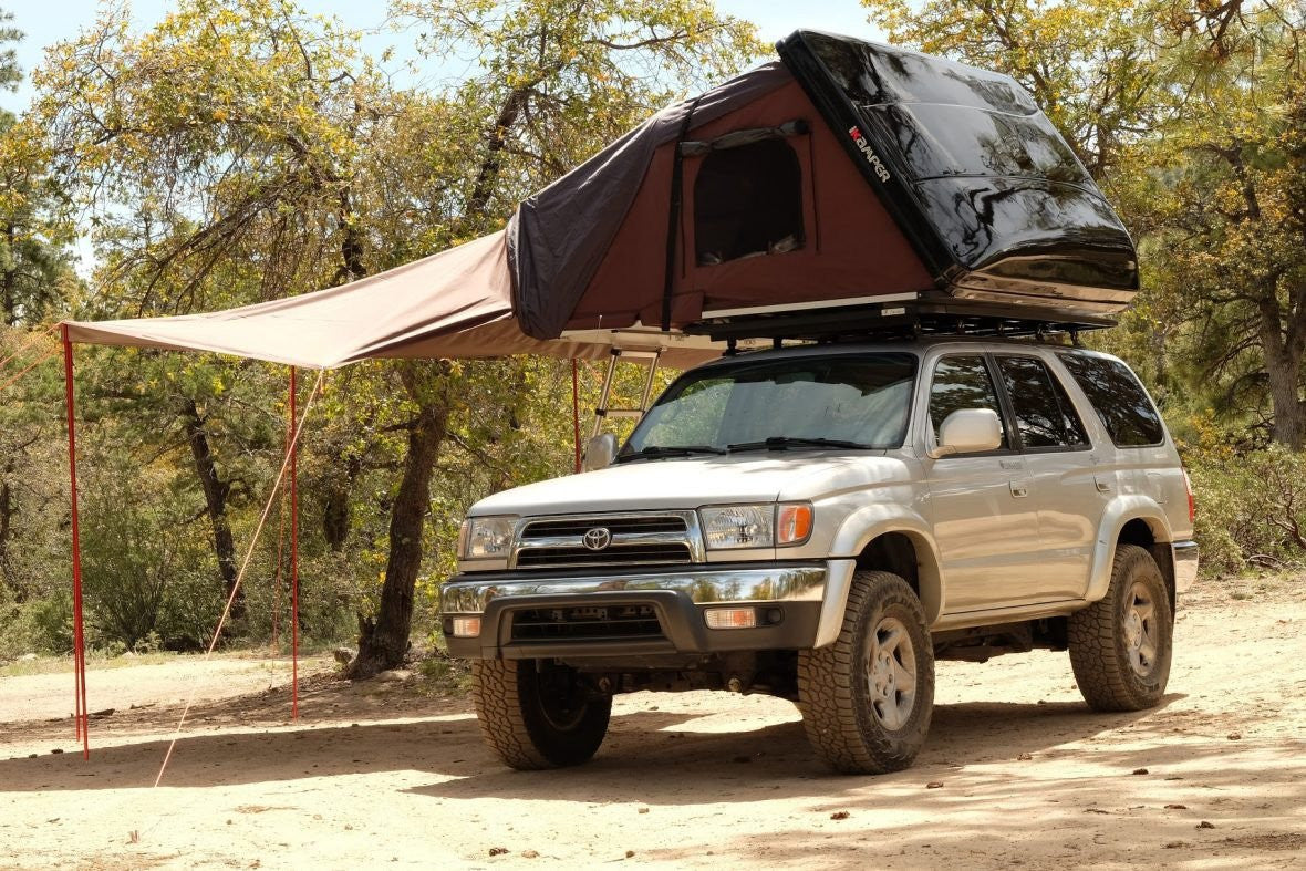 iKamper Skycamp roof top tent shown with awning extension. Awning is supported by two vertical poles and is staked into ground.