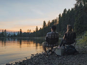 Front Runner Expander Chair all black camping chair shown with people sitting in camping chairs by lake