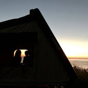 Family in iKamper Skycamp roof top tent shown as silhouette during sunset with ocean view