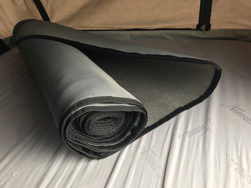 James Baroud Isothermic Kit insulating panels shown prior to installation, rolled up and sitting on built-in mattress inside roof top tent. Panels are thick grey fabric with black trim.