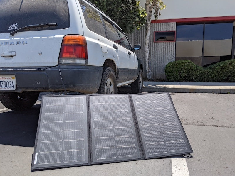 Merlin Solar BXD95 trifold portable solar panel shown deployed next to white Subaru