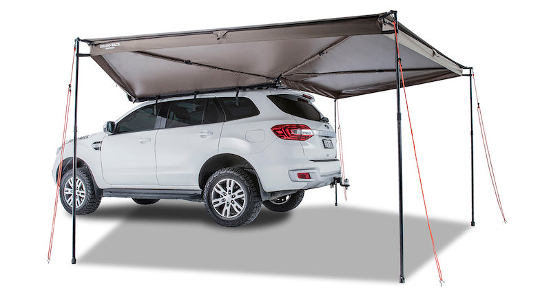 Left Side Mounted Rhino Rack Batwing Awning shown set up with 4 legs extended and tie downs staked in ground