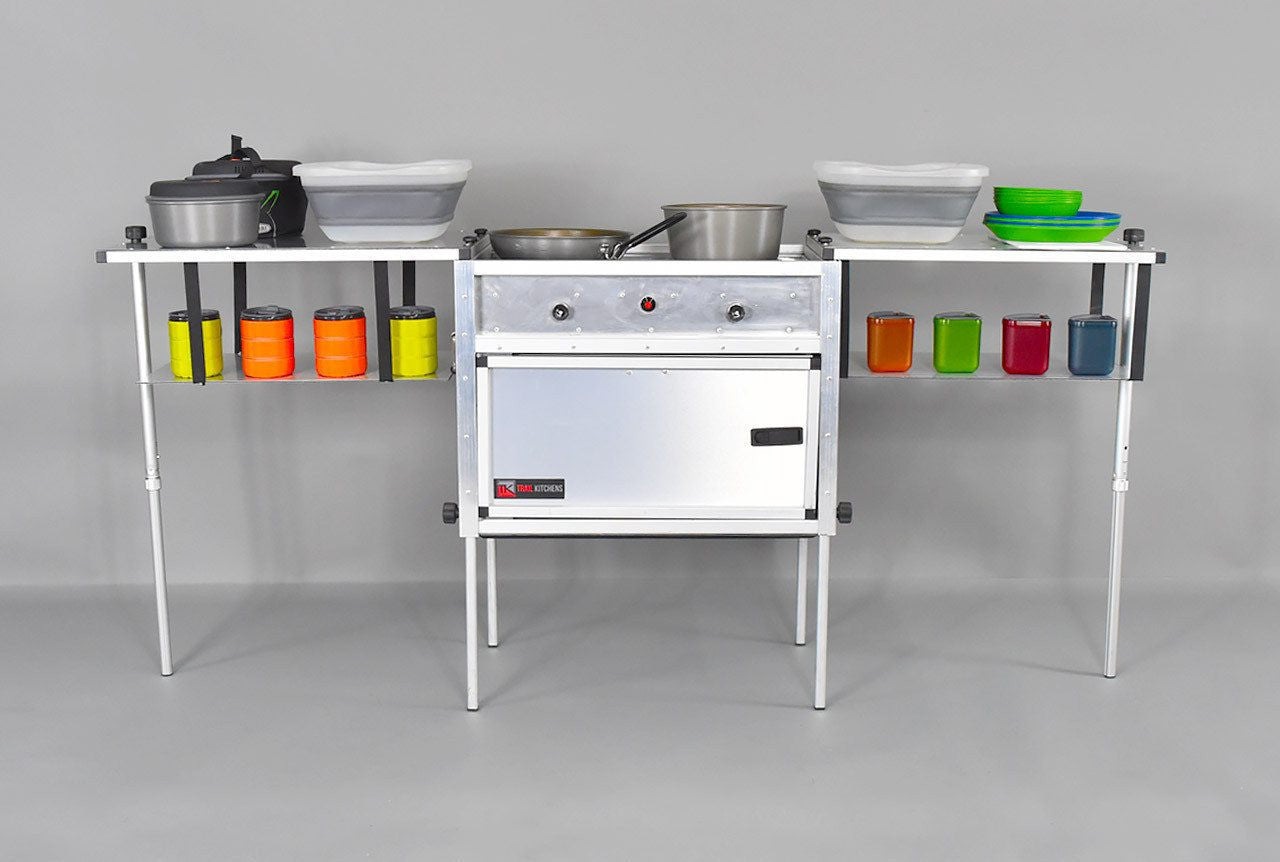 Trail Kitchen Camp Kitchen with Integrated Stove shown assembled with cookware and camping dinnerware on sturdy table and shelving