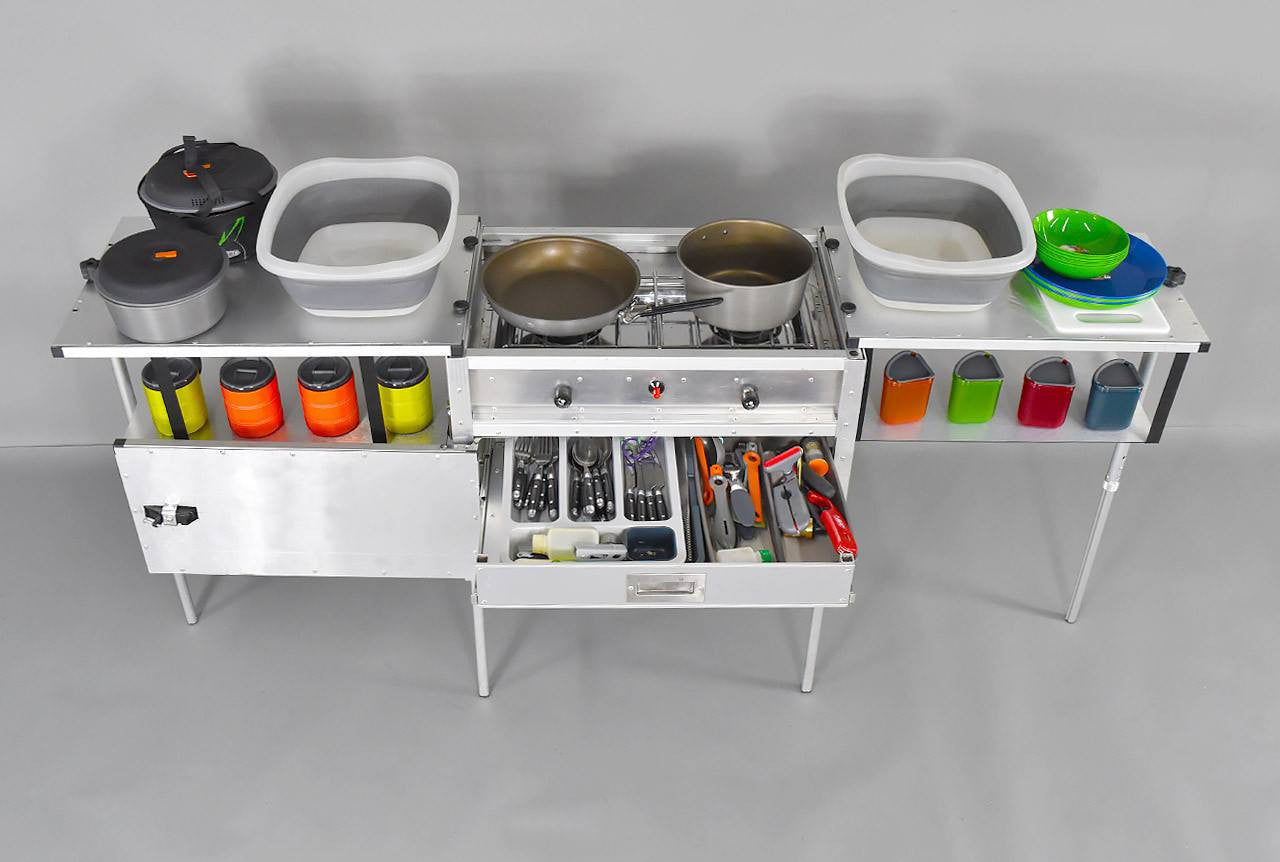 Trail Kitchen Camp Kitchen with Integrated Stove shown loaded with bowls, utensils in a open drawer, and cookware on shelves on either side of the integrated stove