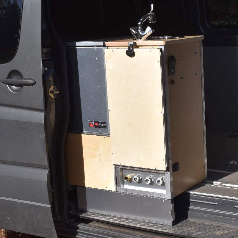 Trail Kitchens Van Kitchen mounted on passenger side of camper van with back unit of kitchen visible showing quick connect fittings for external water source hook up