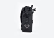Side view of Ubco 2x2 Pannier Bag. Pannier bag is thick black polyester with a handle on top and two wide vertical straps that buckle on the top and there is a small white Ubco logo branding near the bottom of the bag. Clips on the back side of the bag are visible where the bag locks onto pannier rack of the Ubco 2x2