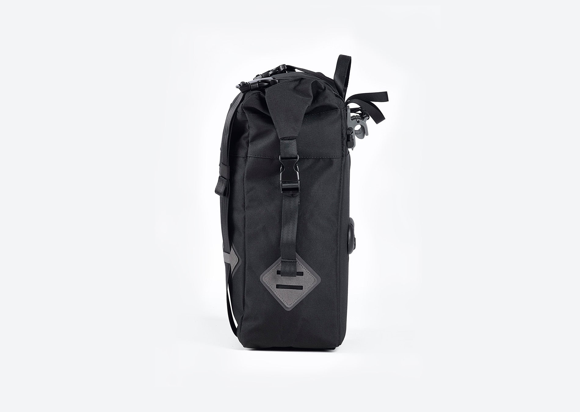 Side view of Ubco 2x2 Pannier Bag. Pannier bag is thick black polyester with a handle on top and two wide vertical straps that buckle on the top and there is a small white Ubco logo branding near the bottom of the bag. Clips on the back side of the bag are visible where the bag locks onto pannier rack of the Ubco 2x2