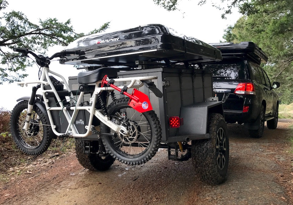 Towball mount bike rack for Ubco 2x2 electric adventure bike shown with bike loaded on rack attached to rear of off road camping trailer